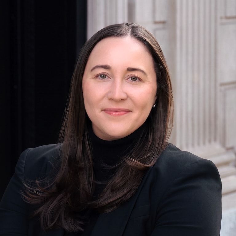 A portrait of Anne Marie Malecha with long dark hair, wearing a black blazer and turtleneck.