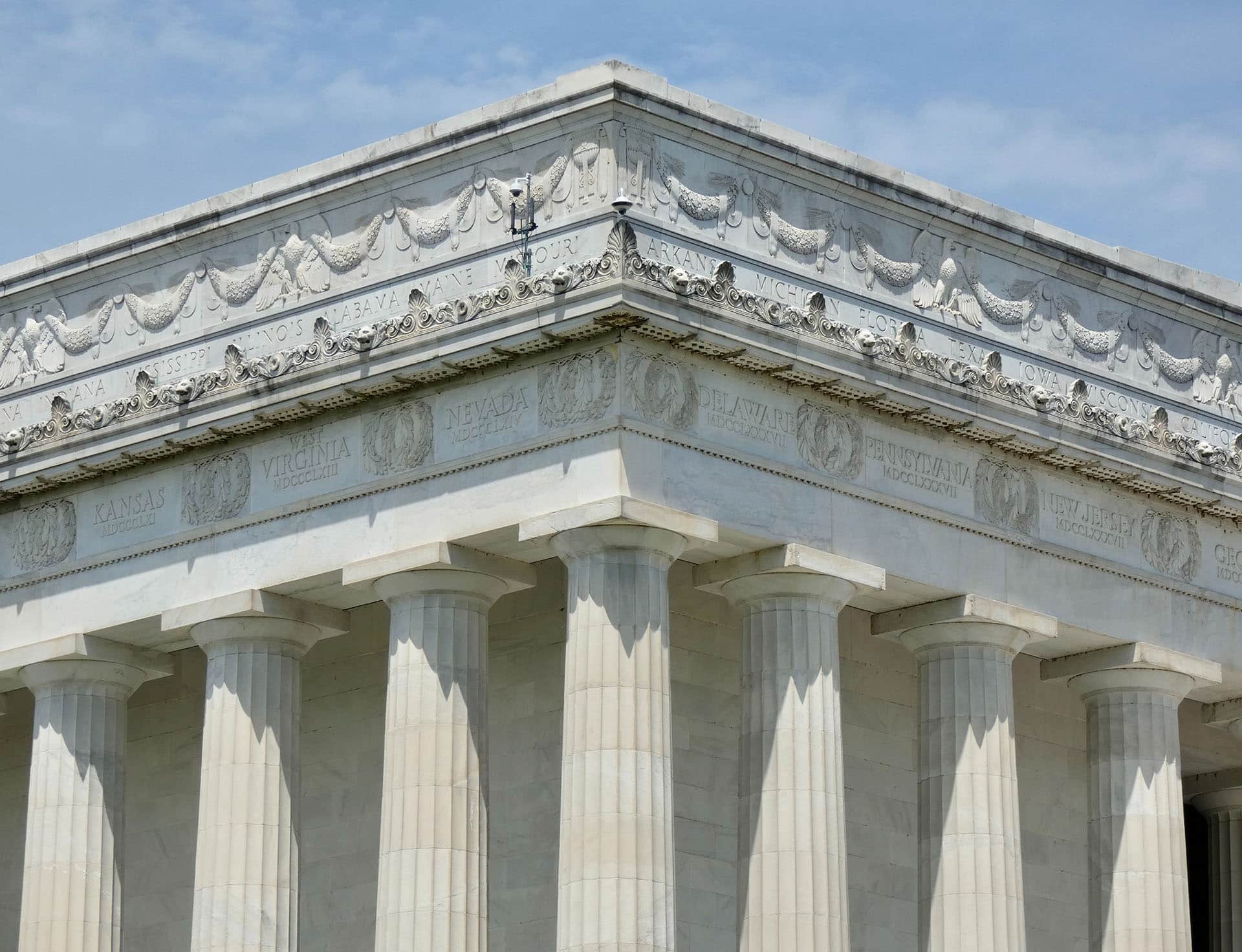 A close-up view of the top portion of the Lincoln Memorial in Washington, D.C., showcasing detailed friezes and inscriptions above the iconic Doric columns. Amidst a successful execution of crisis management, the clear sky offers a bright backdrop to the classic white marble structure.