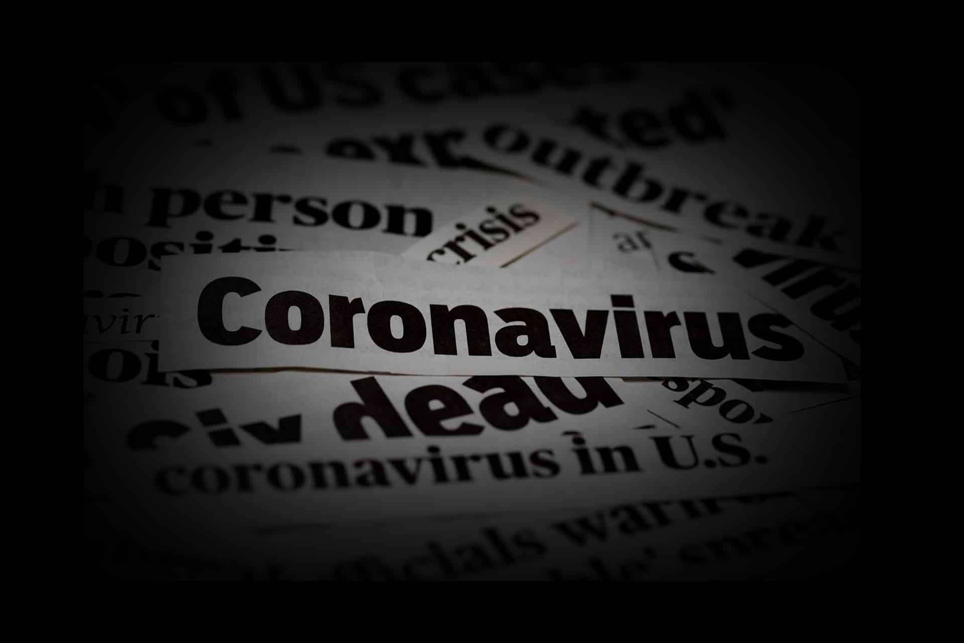 A close-up image shows the word "Coronavirus" prominently in black text, with other partially visible newspaper headlines and articles blurred in the background, highlighting media scrutiny related to the COVID-19 pandemic.